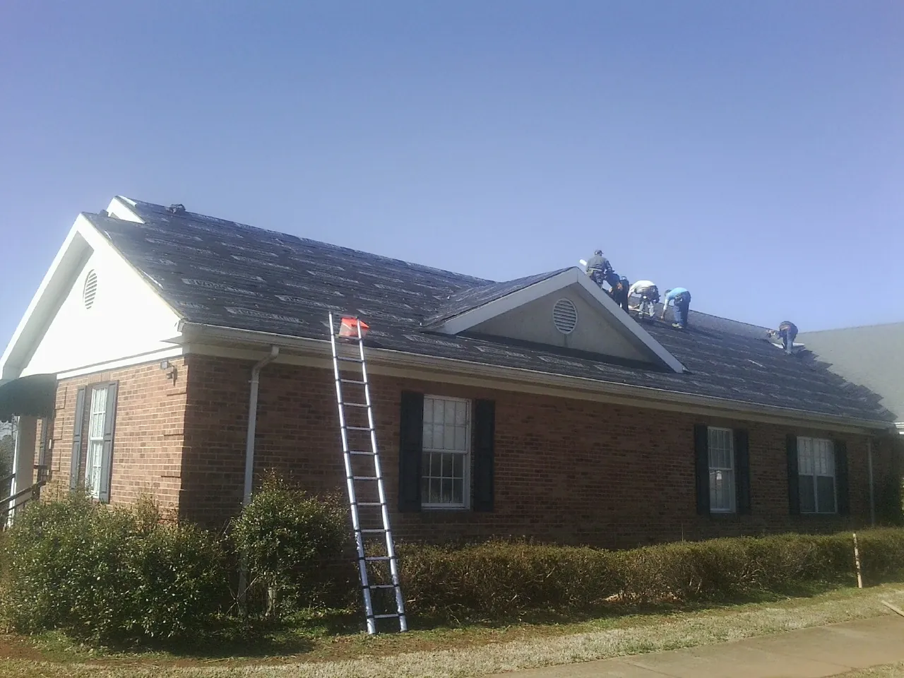 Crew tearing shingles off a brick ranch roof with a ladder set — Metal Roof Repair work by our crew in West Manchester