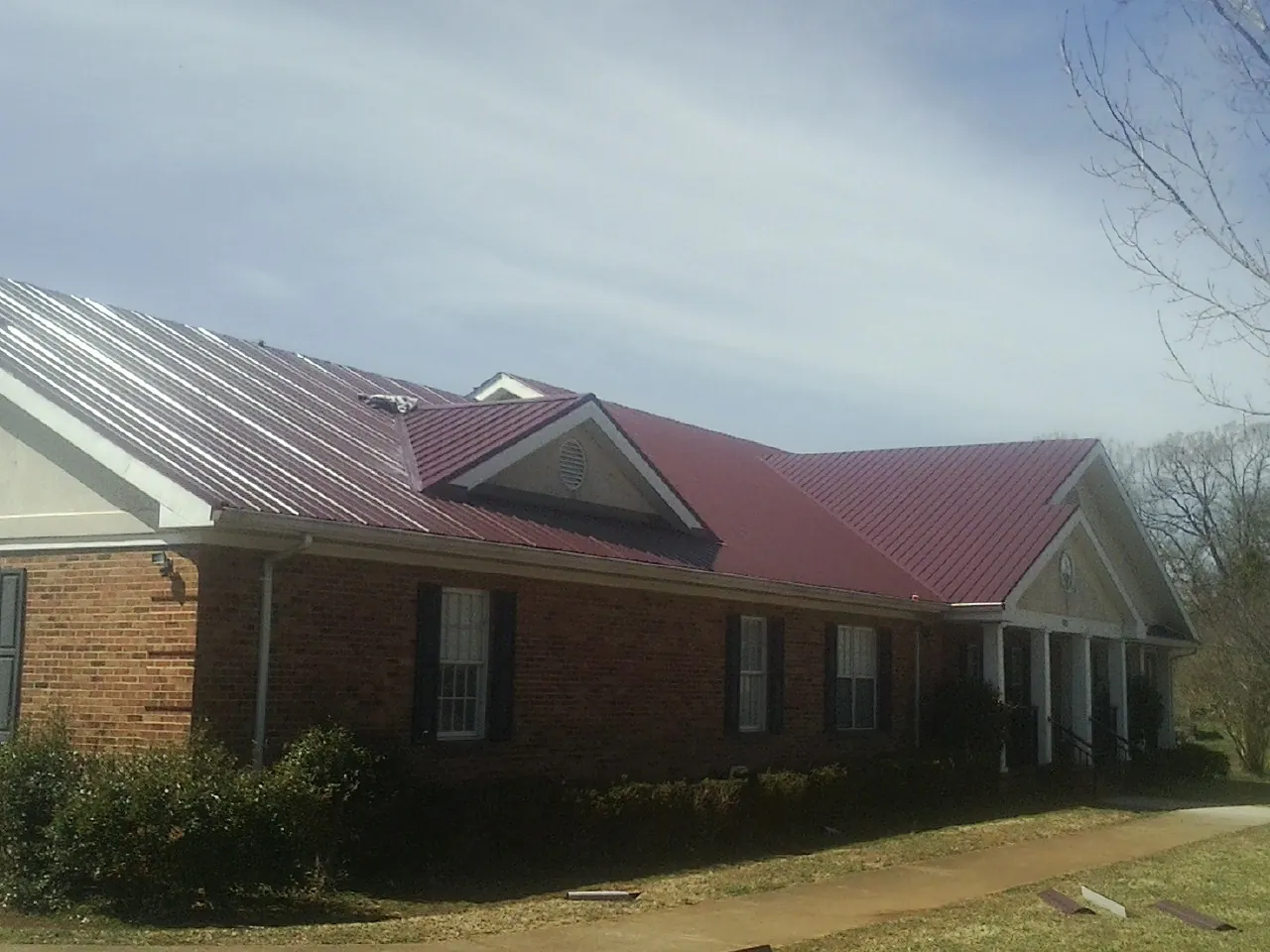 Red metal roof with gabled entries on a long brick building, from a Hail Damage Roof Repair job in West Manchester