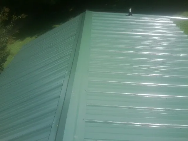 New green metal panels meeting at the ridge of a roof — Flat Roof Repair work by our crew in West Manchester