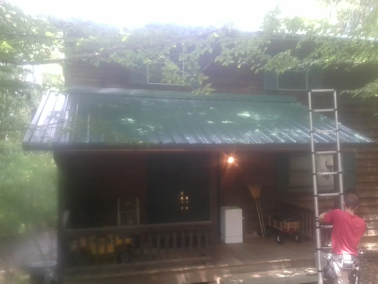 Worker on a ladder at the green porch roof of a wooded cabin in West Manchester