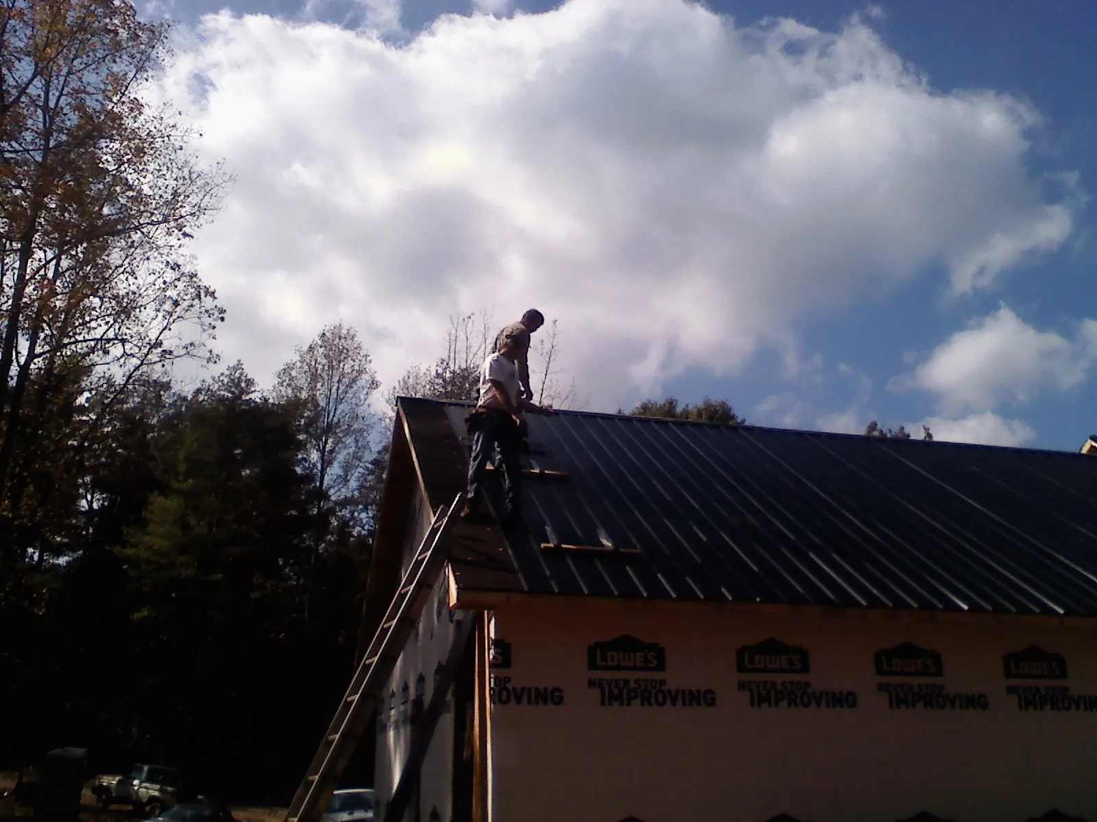 Roofer fastening dark metal panels high against a cloudy sky, from a Roof Inspection job in West Manchester
