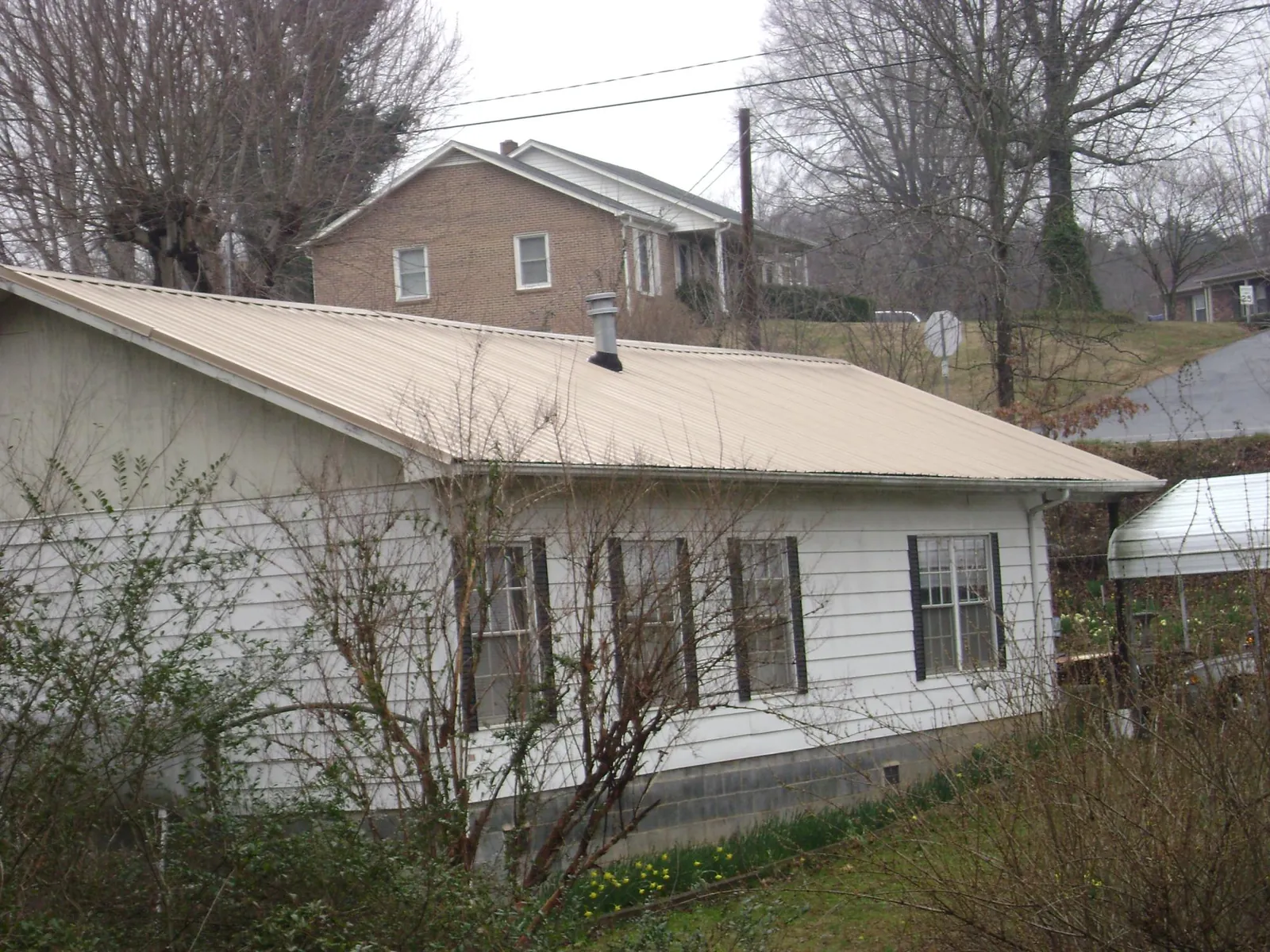 Tan metal roof on a white sided house set into a hillside — Commercial Roofing by Roofing Brothers in West Manchester